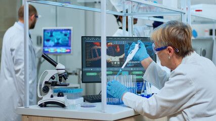 Elderly research scientist using micropipette filling test tubes in modern equipped lab....