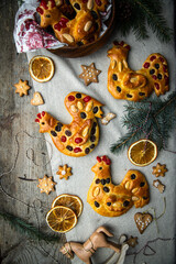 Christmas brioche buns in rooster shape decorated with dried fruits and almonds and gingerbread cookies on wooden table.