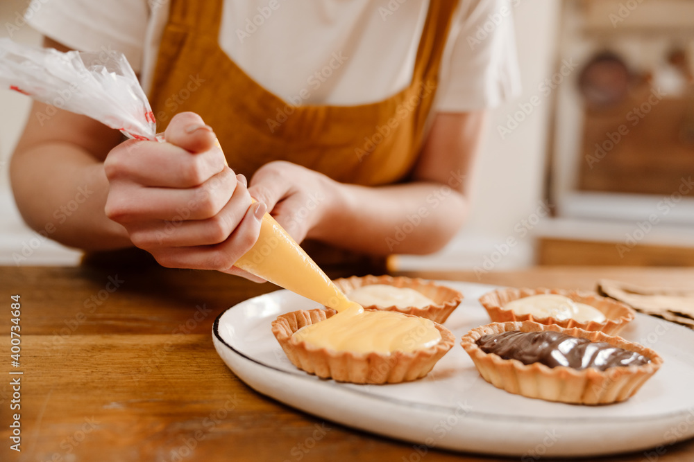 Wall mural Caucasian pastry chef woman making tarts with cream at cozy kitchen