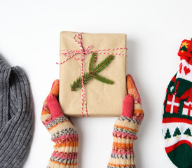 female hands in knitted mittens hold a box wrapped in brown paper and tied with a rope