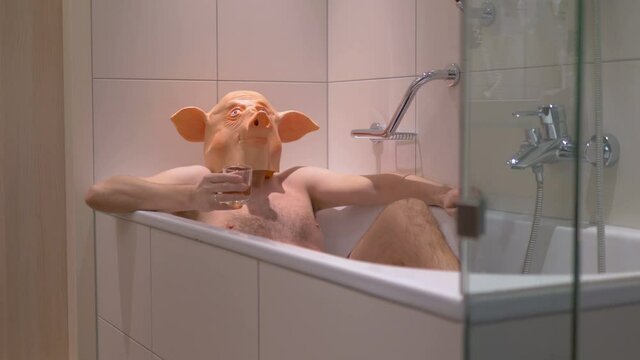 Man in a pig mask relaxing in bathtub and drinking cocktail after work in 4k slow motion 60fps