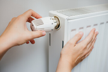 Close up shot of Caucasian female's hand adjusting radiator temperature using thermostat. Home with...