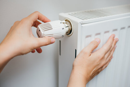 Close up shot of Caucasian female's hand adjusting radiator temperature using thermostat. Home with central heating.