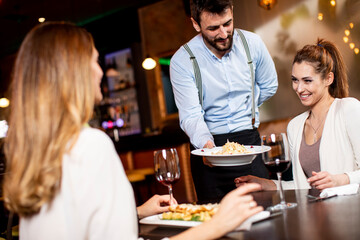 Young waiter serving food to female customers in the restaurant