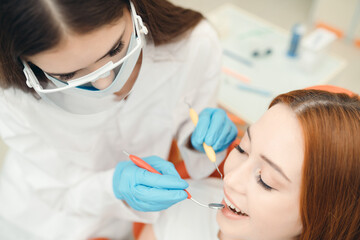 Fototapeta premium The dentist makes teeth cleaning to a beautiful red-haired girl with the help of special tools