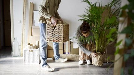 joyful young family of happy guy and woman wearing casual clothes carries boxes with different belongings. Couple celebrating moving day hugging and kissing give five together into large room 