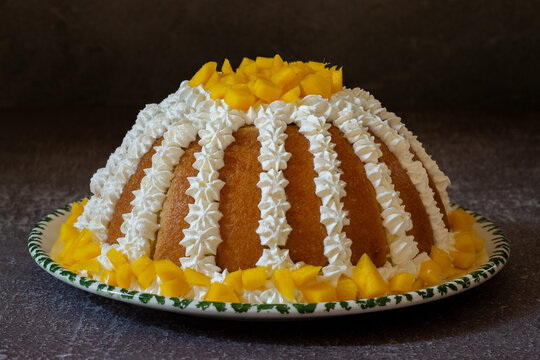 Zuccotto with mango. Traditional Italian cake on a white and green plate decorated with cream and mango on top, on a gray background.