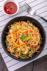 Hakka noodles with sauce and veggies served in a black bowl with fork