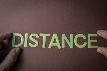 Human fingers holding the word Distance written with plastic letters on brown paper background, concept