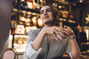Pensive female customer with caffeine beverage in hand thoughtful looking away pondering on sweet taste of coffee, contemplative smart casual woman with tea cup thinking about leisure pastime