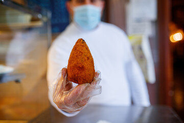 Arancino di riso mantenuto da una mano con guanto