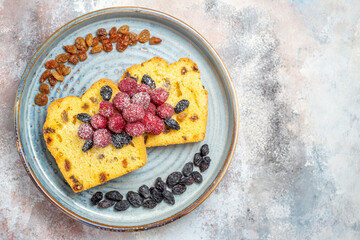top view raisin cake slices with raisins and raspberries on blue oval plate on marble background with copy space