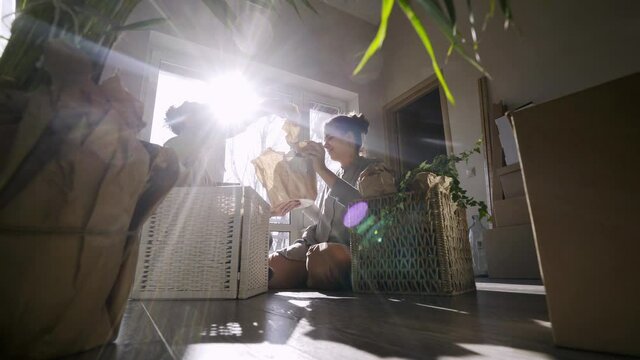 Cheerful couple sit among boxes with different belongings in bright sun light. Man and woman unwrap things in our new flat, kissing and hugging. concept moving day