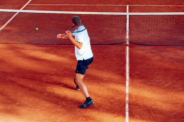 Obraz premium Back view of a man playing tennis on tennis court