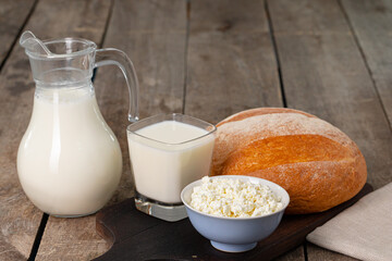 Glass jar of milk, bowl of cottage cheese and bread on wooden table