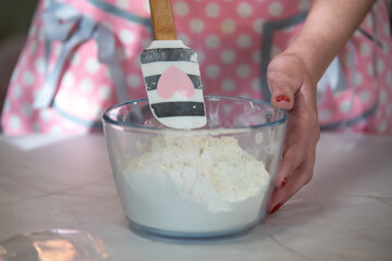 woman mixing flour in a glass bowl with a pink apron at home