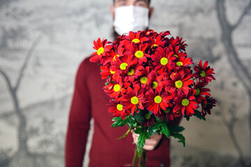 Young male with protective face mask for Coronavirus with flower bouquet, Red daisies for romantic Valentines Day or Birthday, present and covid-19 concept