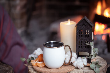 Cozy composition with a cup, candle and tangerines on a blurred background of a burning fireplace copy space.