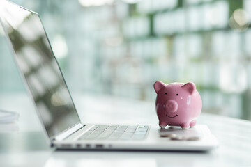 Pink piggy bank on laptop key board on wooden table and blurred background indoors-Concept of money...