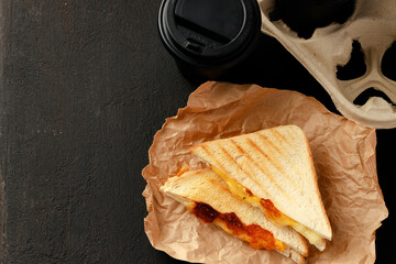 Toasted sandwich in craft paper with cup of coffee on table