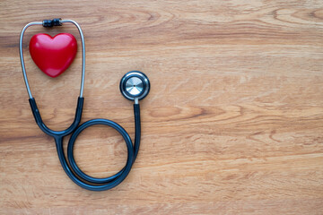 Black stethoscope with red heart of doctor for checkup on wood table background. Stethoscope equipment of medical use to diagnose hear sound. Health care and cardiology concept with copy space.