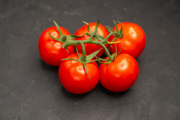 Overhead view of five fresh tomatoes with stems on dark background in horizontal view