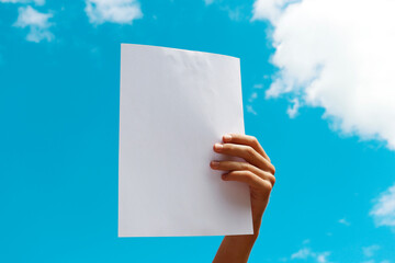 a blank sheet of paper in the hands of a young guy against a blue sky with clouds