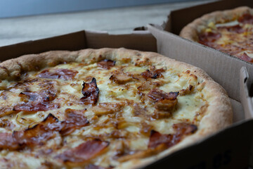 Closeup view of two pizzas on cardboard boxes.Carbonara pizza with caramelized onion and bacon and Hawaiian pizza.