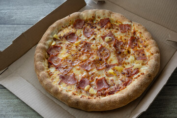 Delicious fresh pizza with bacon, cheese and pineapple on cardboard box.Hawaiian pizza.