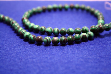 Green beads on a blue felt background.