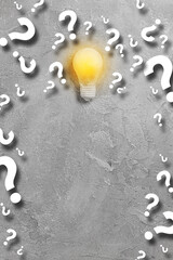 Idea glowing light bulb, a lot of curtain question symbols on gray concrete background. Minimal...