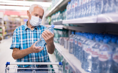 elderly european man in mask with covid protection selects bottled water in department of...