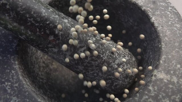 Spicy exotic white peppercorns are falling into the grey stone mortar in slow motion