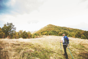 Obraz premium Man hiking on autumn day through beautiful nature landscape. Misty Mountain Peak. Rear View. Cloudy sky in the background.
