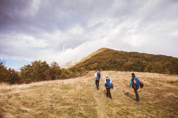 Group of active people hiking on autumn day through beautiful nature landscape. Misty Mountain Peak. Rear View. Cloudy sky in the background.