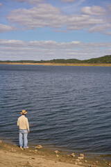 Fototapeta na wymiar Caucasian senior man fishing with a straw hat on a dam lake reservoir in Alentejo, Portugal