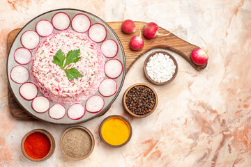Above view of delicious chicken salad with beet on a gray plate on wooden cutting board and radishes with different spices on mixed color background