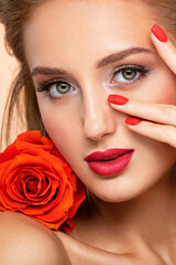 Beautiful young woman with a red flower and nails near face. Art portrait of an attractive model