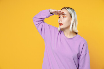 Young blonde caucasian woman with bob haircut bright makeup wearing casual basic purple shirt holding hand at forehead looking far away distance isolated on yellow color background studio portrait
