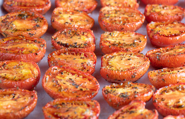 Roasted tomatoes are lined up on a baking sheet covered in spices
