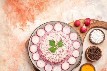 Obraz na płótnie Canvas Above view of delicious chicken salad with beet on a gray plate on wooden cutting board and radishes with different spices on mixed color background