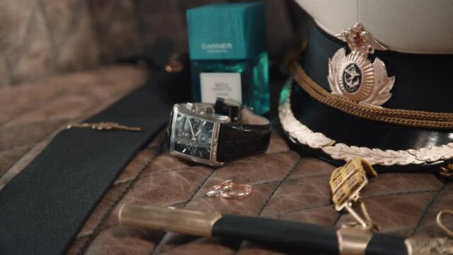Wedding rings, perfume and seaman hat on table. Expensive watch and belt. Sailor themed ceremony