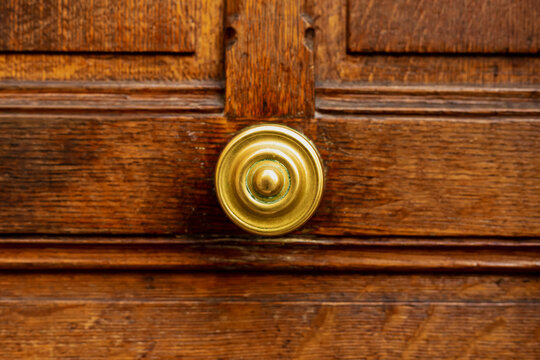 Old round door handle on old wooden brown door. Close up Paris, France. Gold brass details on old wooden door. Handle on brown old wooden shabby vintage door.