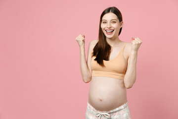 Fototapeta na wymiar Pregnant woman future mom in basic top with belly tummy with baby doing winner gesture say Yes clenching fists isolated on pastel pink background studio. Maternity family pregnancy gynecology concept.