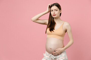 Tired sad young pregnant woman future mom in basic top stroking keeping hands on belly stomach tummy with baby isolated on pastel pink background studio. Maternity family pregnancy gynecology concept.