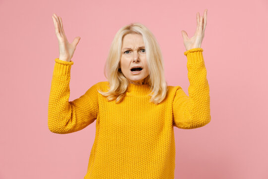 Angry Irritated Elderly Gray-haired Blonde Woman Lady 40s 50s Years Old In Yellow Casual Sweater Standing Spreading Hands Swearing Screaming Isolated On Pastel Pink Color Background Studio Portrait.