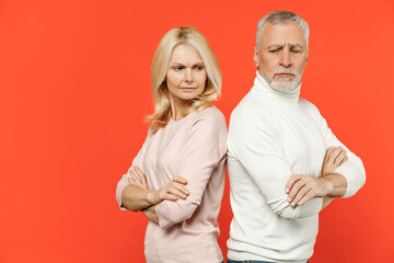Side view of displeased offended couple friends elderly gray-haired man blonde woman in white pink clothes standing back to back holding hands crossed isolated on orange background studio portrait.