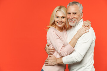 Smiling beautiful pretty couple two friends elderly gray-haired man blonde woman in white pink casual clothes standing hugging looking camera isolated on bright orange wall background studio portrait.