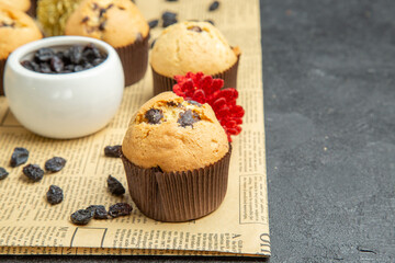 Close up view of small cupcakes black raisin and accessories on newspaper on dark isolated background