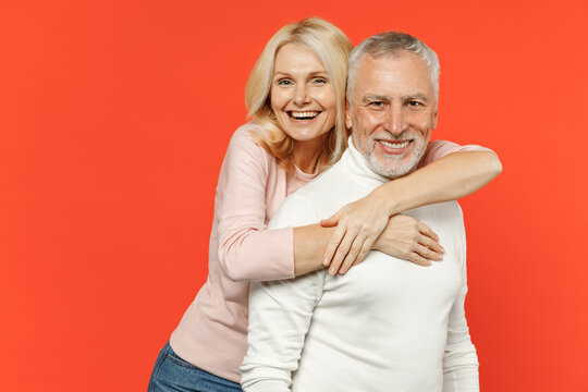 Cheerful laughing funny couple two friends elderly gray-haired man blonde woman in white pink casual clothes standing hugging looking camera isolated on bright orange color background studio portrait.